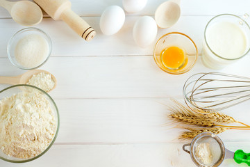 Fototapeta premium Cooking bread in the kitchen from the ingredients: flour, sugar, salt, eggs. Roller, wooden spoons, corolla on a white wooden background