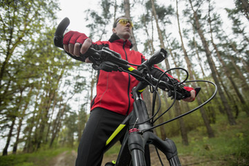 Young attractive man wears red suit ride the bike on the forest road