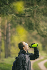Young attractive man wears dark suit drink water from sport bottle in the forest