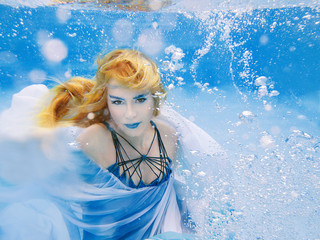 Underwater fashion portrait of beautiful blonde young woman in blue dress 