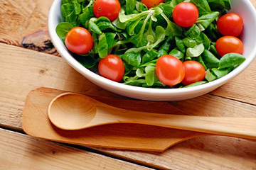 Cherry tomatoes and basil salad in a white cup on a wooden table.