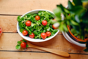 Cherry tomatoes and basil salad in a white cup on a wooden table.
