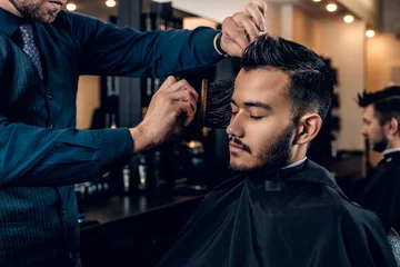 Crédence de cuisine en verre imprimé Salon de coiffure Hairdresser doing haircut to a bearded man in a barbershop.