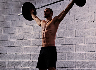 The athletic shirtless male holds a barbell under his head.