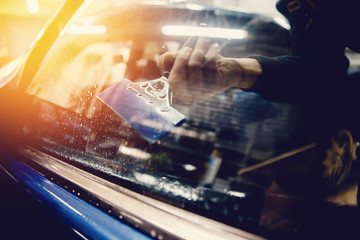 Master installs a tint film for the car glass with a hairdryer and spatula with glare of light....