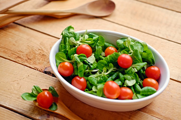 Cherry tomatoes and basil salad on a plate with a pot on a wooden table.