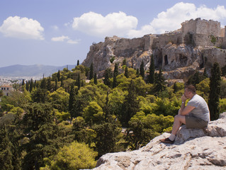 Modern man sits at the foot of the Ancient Acropolis in Greece in Athens and thinking about the...