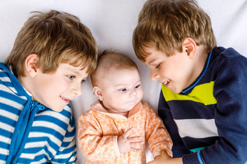 Two happy little preschool kids boys with newborn baby girl