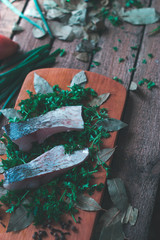 Sliced fresh fish with spices and parsley on a wooden board.