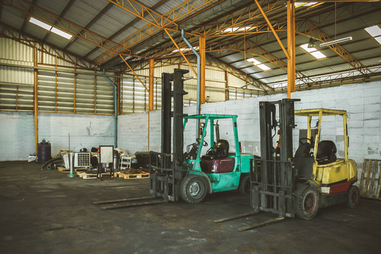 Old forklift, with no driver, parked inside an industrial hall, with industrial machinery and a roll of metal sheet in the background