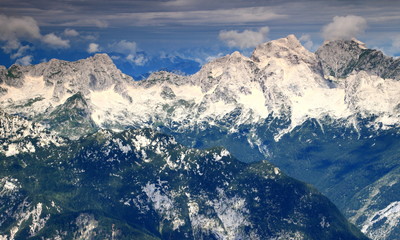 Dark green pine forested ridges over Trenta Valley with mighty Jalovec and Mangart peaks, Julian Alps, Triglav National Park, Slovenia, with Italy in clouds in the background