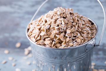 Raw oat flakes in a bucket on wooden background