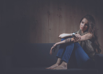 Portrait of elegant woman sitting on black sofa wearing a blue jeans and fur vest