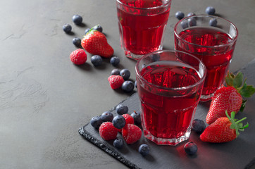 Three glasses of fresh juice made of strawberries, raspberries and blueberries. Slate plate, copy...