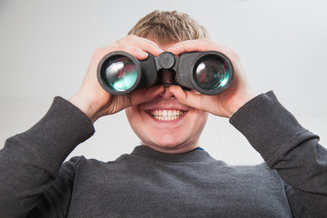 Young handsome man looking through window with binocular glasses