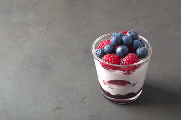 Glass of homemade yogurt with fresh blueberries and raspberries. Gray background, copy space