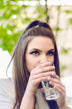 beautiful young girl or woman sitting in a cafe and drinking a glass of water, summer days and hydration