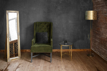 Dark green soft armchair near plaster wall. Arm-chair with fabric upholstery and big vintage mirror in loft style interior