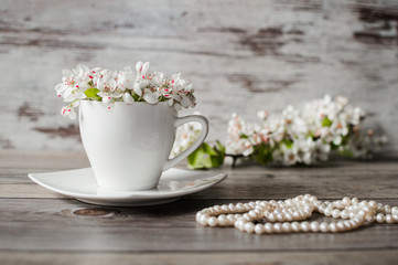 Morning cup of blooming white flowers of pear tree, beads from pearls on a gray wooden background.