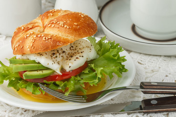 Breakfast. Bun with sesame seeds, poached egg, avocado, tomato and greens. Selective focus