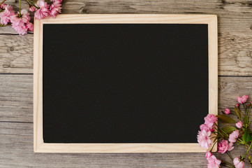 Copy space on a black blackboard with beautiful branches of pink flowering sakura at the corners of the board.