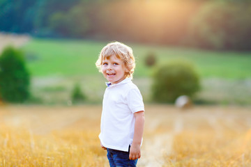 Naklejka na ściany i meble Happy blond kid boy enjoying sunset in wheat field.
