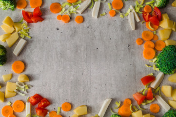 Frame of juicy sliced vegetables on gray stone background. Carrots, broccoli, parsley root, leek, tomato, potatoes are so appetizing and useful.