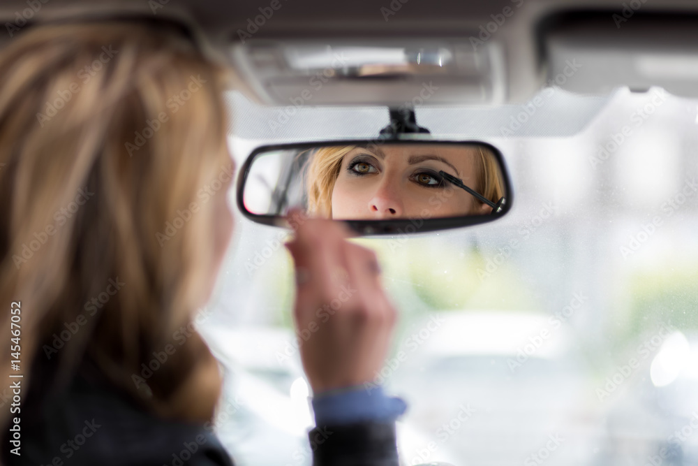 Wall mural Beautiful young woman applying make-up while driving car