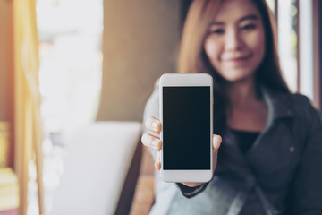 Mockup image of a beautiful woman with smiley face holding and showing white mobile phone with blank black screen in vintage cafe