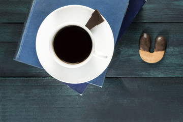 Coffee cup with old books, chocolate piece and cookie