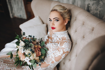 Beautiful bride in a lace dress with an original wedding bouquet in a vintage interior.
