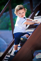 Little handsome boy climbs on the wooden stairs to the top.