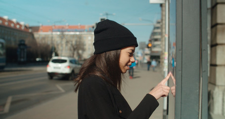 Fototapeta premium Young woman checking a bus timetable in a city street.