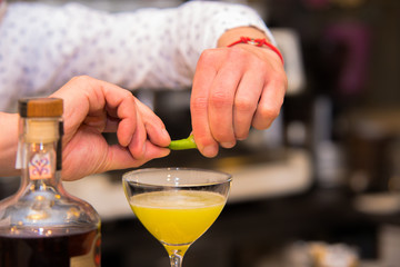Closeup of barman hand putting lemon peel on a glass to prepare cocktail.