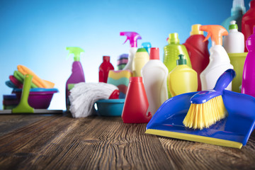 Spring cleanup theme. Variety of colorful house cleaning products on a rustic wooden table and blue background. 