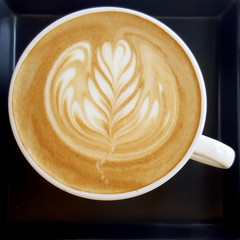 Top view of a mug of latte art coffee on black background.