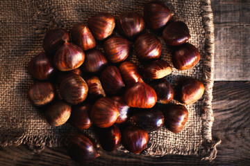 Fresh chestnuts on brown sack bag. Big ripe tasty Chest nuts  on old wooden table with copy space, close up.