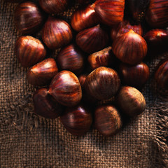 Fresh chestnuts on brown sack bag. Big ripe tasty Chest nuts  on old wooden table with copy space, close up.