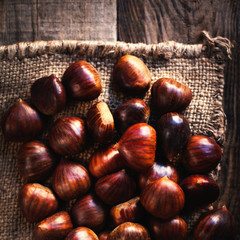 Heap  of edible fresh chestnuts on old wooden table. Group of ripe big chestnuts with copy space, macro