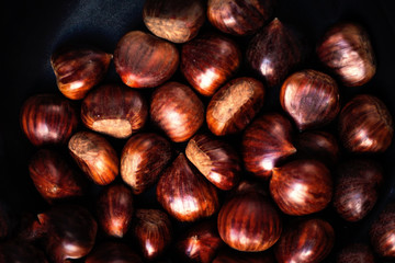 Heap  of edible fresh chestnuts on old wooden table. Group of ripe big chestnuts with copy space, macro