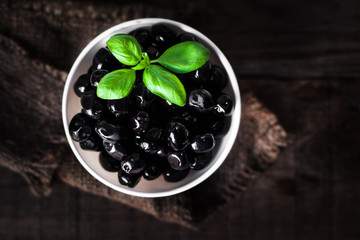 Black olives  on a white  plate on dark wooden board, top view with copyspace.