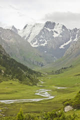 Fototapeta na wymiar river valley with snow-covered mountains and green fields and forest on slopes