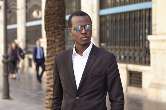 Businesspeople, fashion and modern urban lifestyle concept. Well-dressed successful banker in stylish eyewear and suit standing outdoors, looking serious while waiting for business partners for lunch