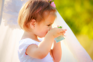 Little beautiful girl in a white dress drinks from a cup.