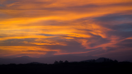 Dramatic sunset orange cloudy sky with tree and hill line silhouette