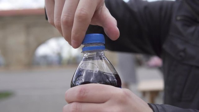 Closeup view of man's hands unscrewing the top from a soda bottle in the street cafe. Shot in 4k