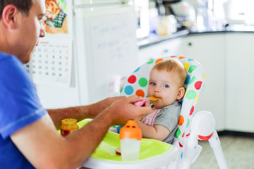 Young caring father feeding cute baby daughte at home. Family concept, soft selective focus
