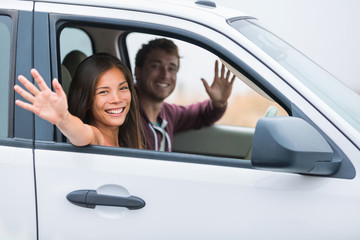 Happy multiracial couple on car travel together on summer vacation. Joyful young people smiling waving hello driving on road trip holidays. New young owners.