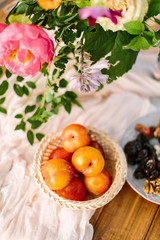 Fototapeta na wymiar picnic, food, summer, holiday concept - close-up on the festively decorated table with beautiful pink peony and white rose flowers, fresh and dried fruits, nectarines, walnuts, prunes, tableware
