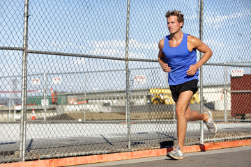 Runner man running - urban city lifestyle. Young sports male athlete jogging in grunge fence background outdoors in summer activewear. Active living.